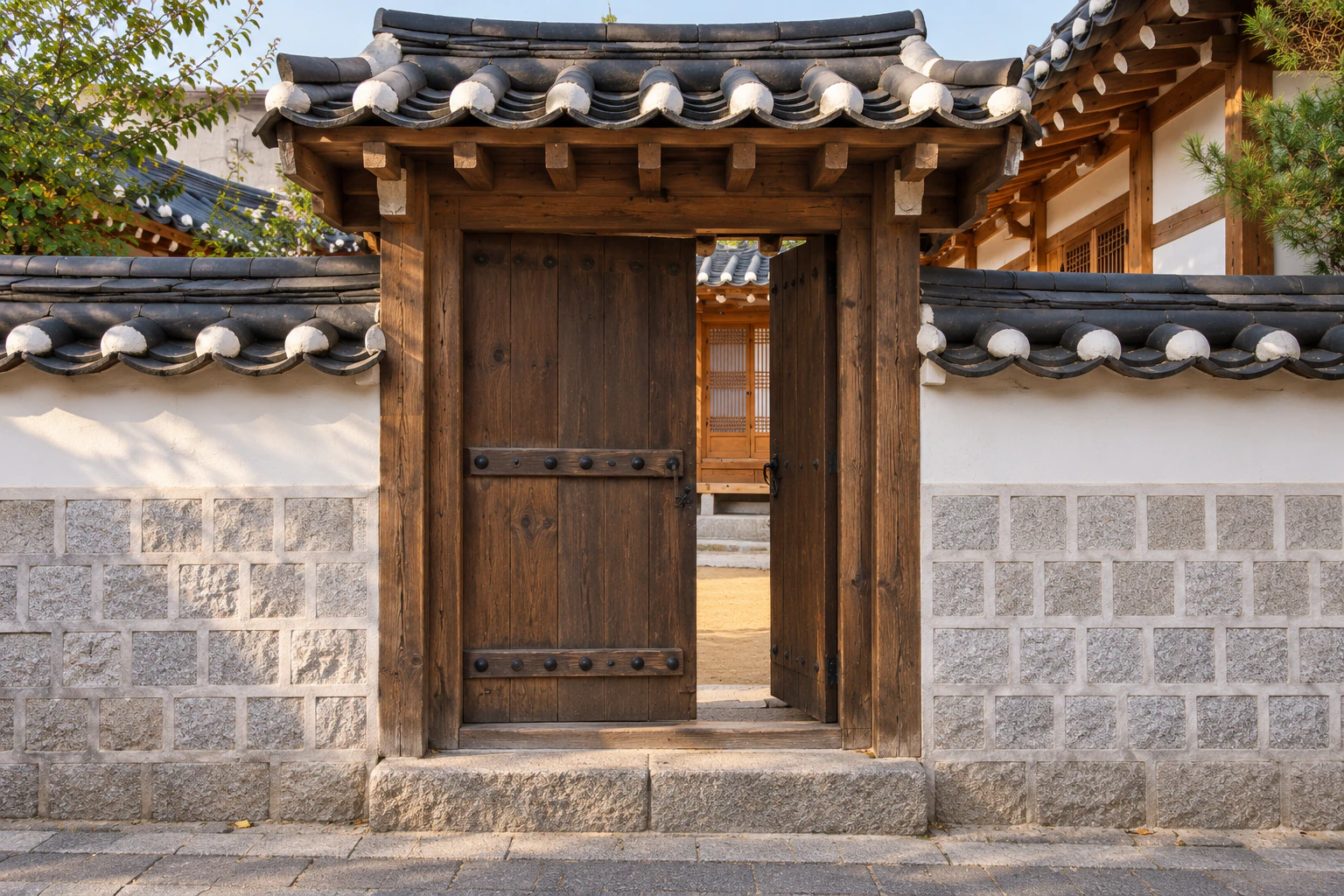 Close view of a hanok gate with wooden leaves and a tiled roof, white plaster and granite blocks. Editorial image.