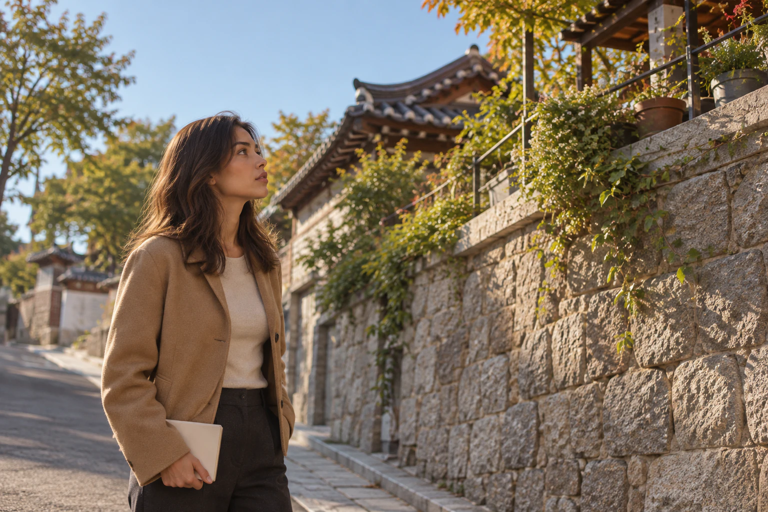 站在窄人行道上、抬頭看對街擋土牆上露臺的年輕女子側臉，駝色外套。編輯圖片。