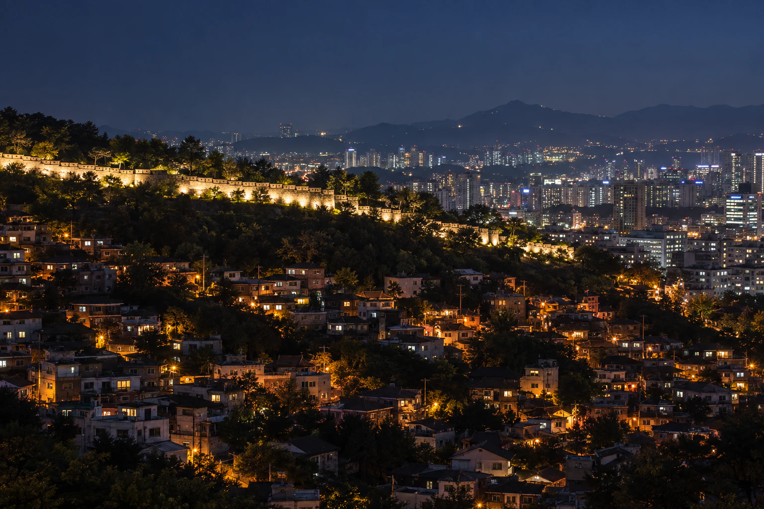 A lit stone wall winding along a ridge at night above city lights. No people. Editorial image.
