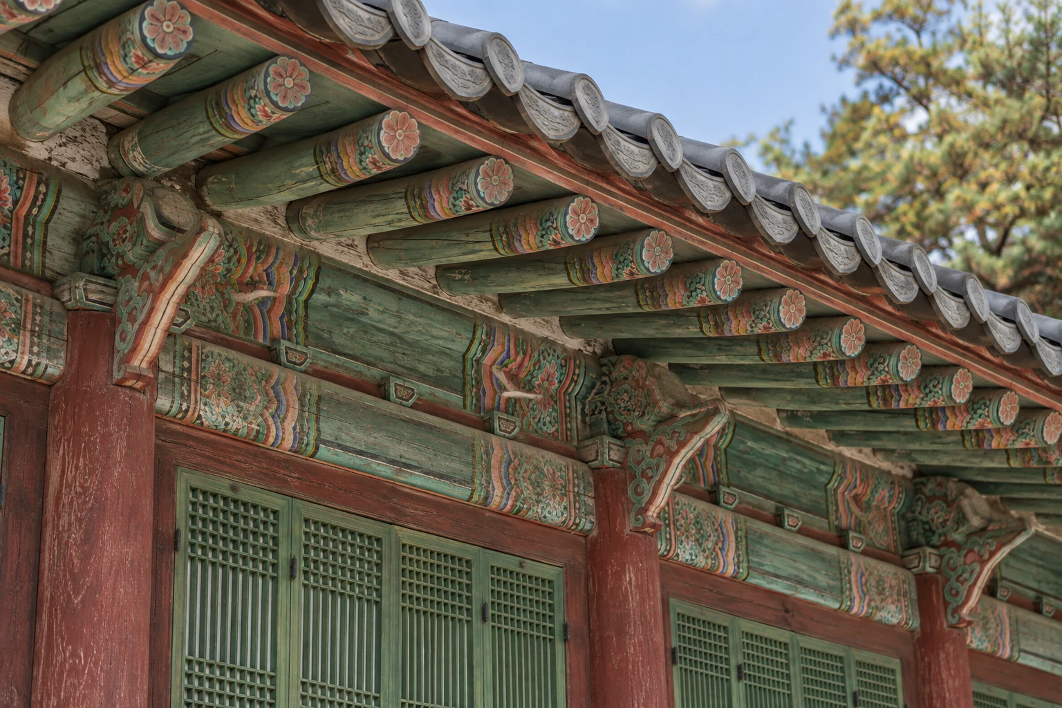 A close view of colourful painted brackets under the eaves and green latticed doors. No people. No lettering. Editorial image.