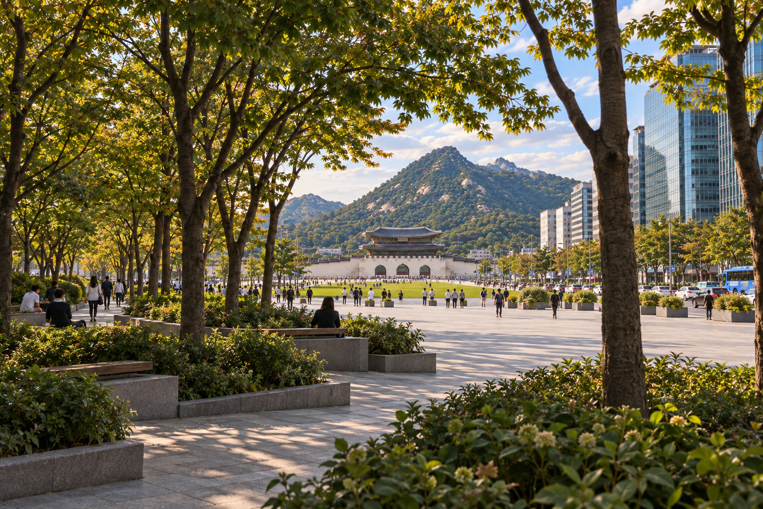 Broadleaf trees, planting beds and benches in dappled shade at the edge of a square, the bright square, a palace gate and a mountain seen through the trees. Editorial image.