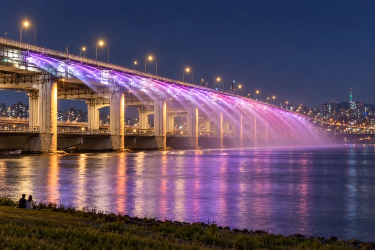 盤浦大橋、夜7時30分を待つ川辺 — マヤが高速ターミナル駅から川辺へ下り、夕方の芝生と潜水橋を通って、月光レインボー噴水の夜の最初の回を待つ一日
