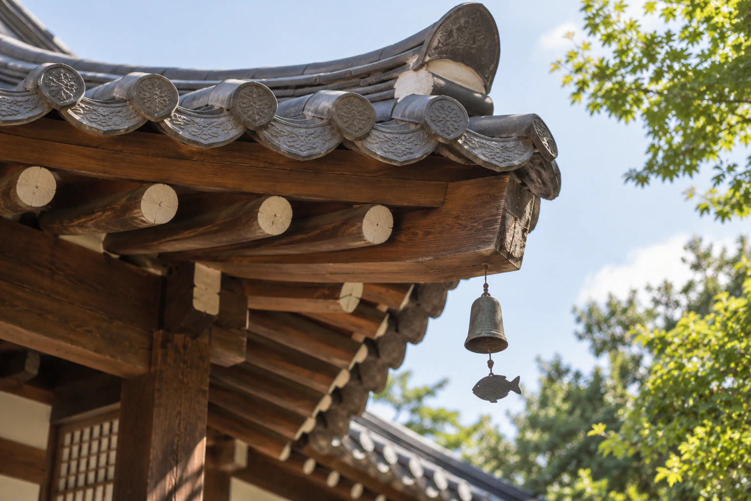 A small metal wind chime hanging at the end of a hanok's eaves, close up. Editorial image.