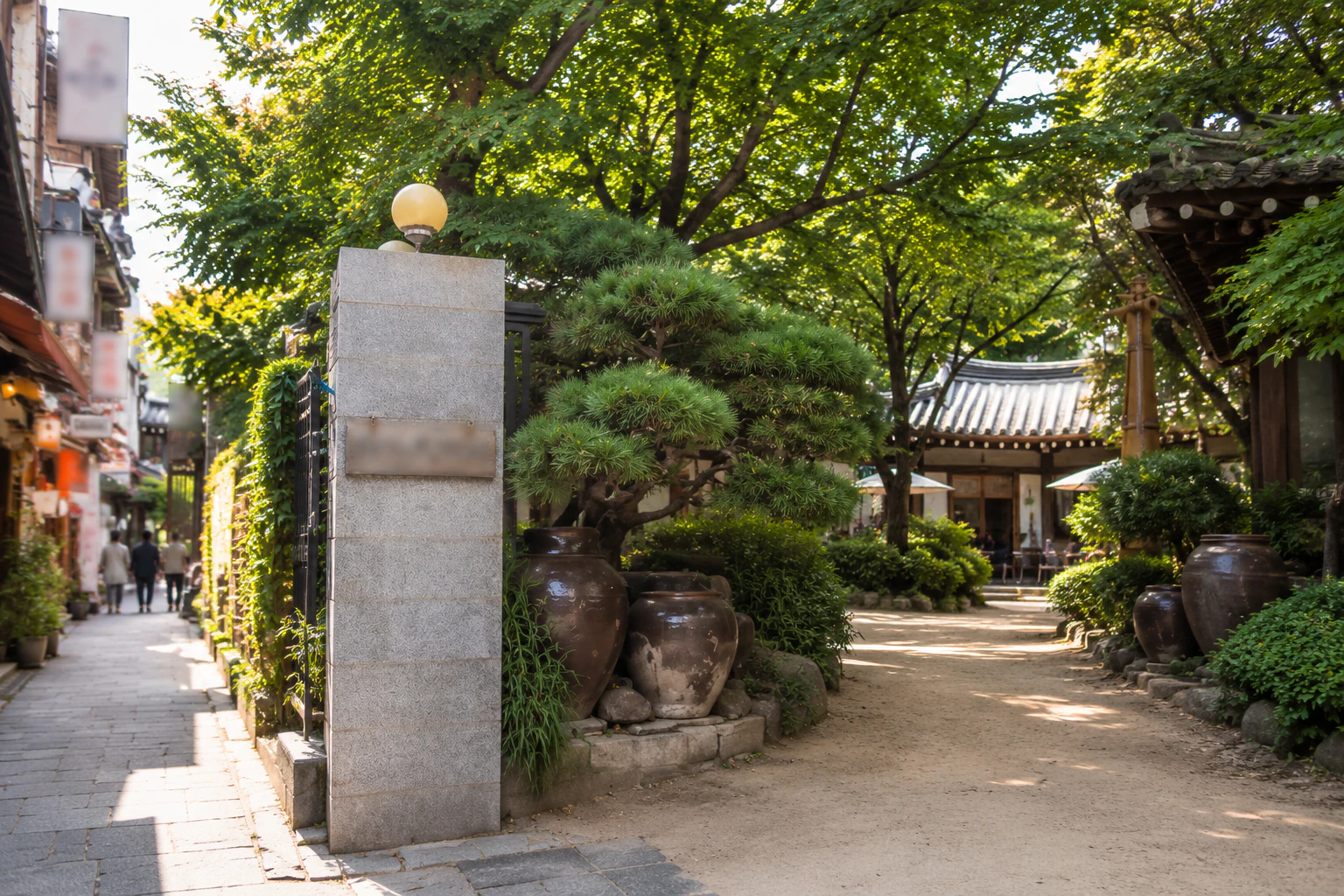 The museum entrance with a granite gatepost, big onggi jars and a clipped pine, the sandy path leading in to a hanok in the courtyard. Editorial image.