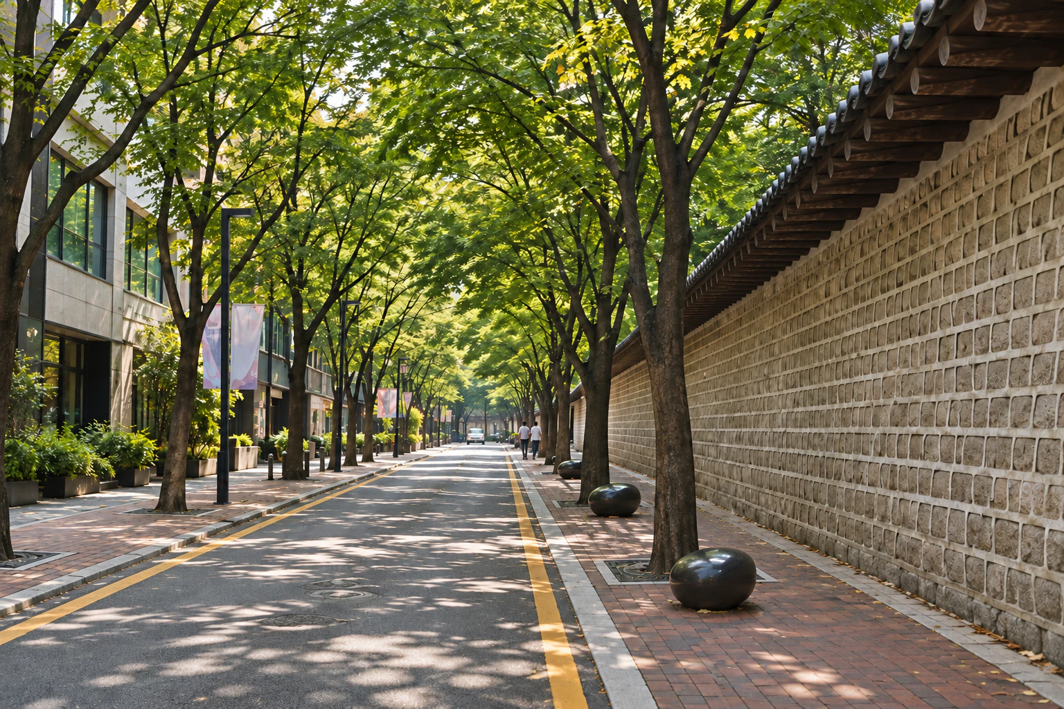 大きな街路樹が影をつくる狭い道、右に花崗岩の塀と黒い瓦、塀側の歩道は赤茶色