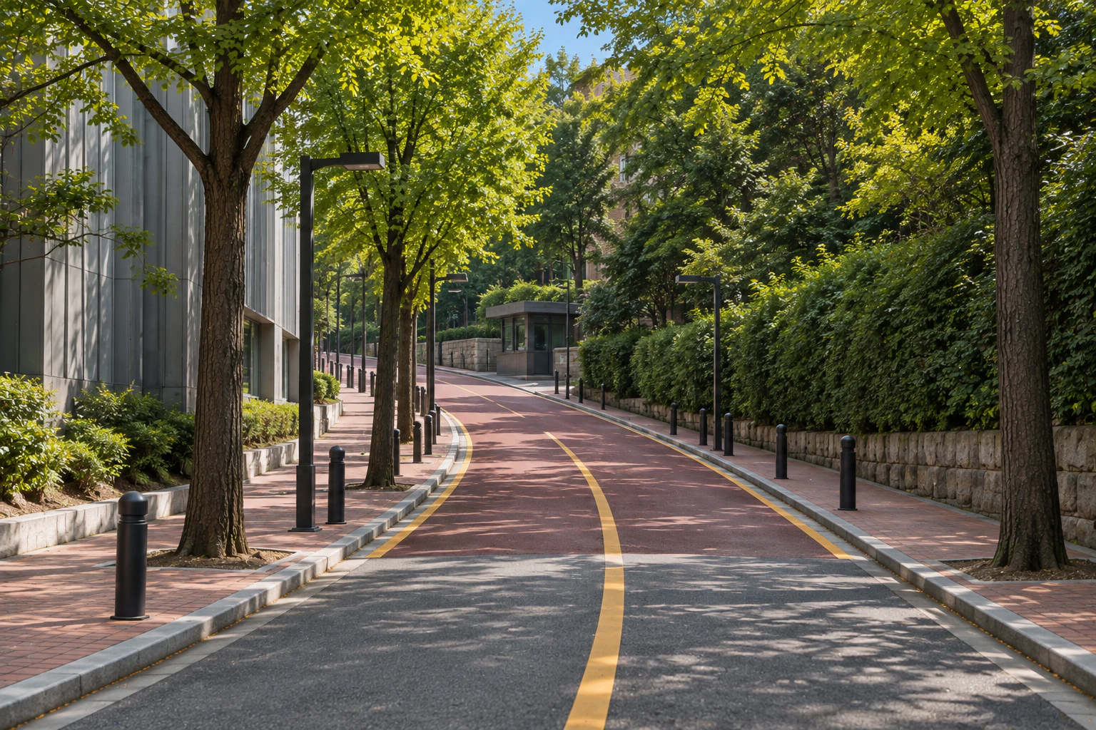 A narrow street bending uphill as its surface turns red, a grey-panelled building on the left and a tree fence on the right.