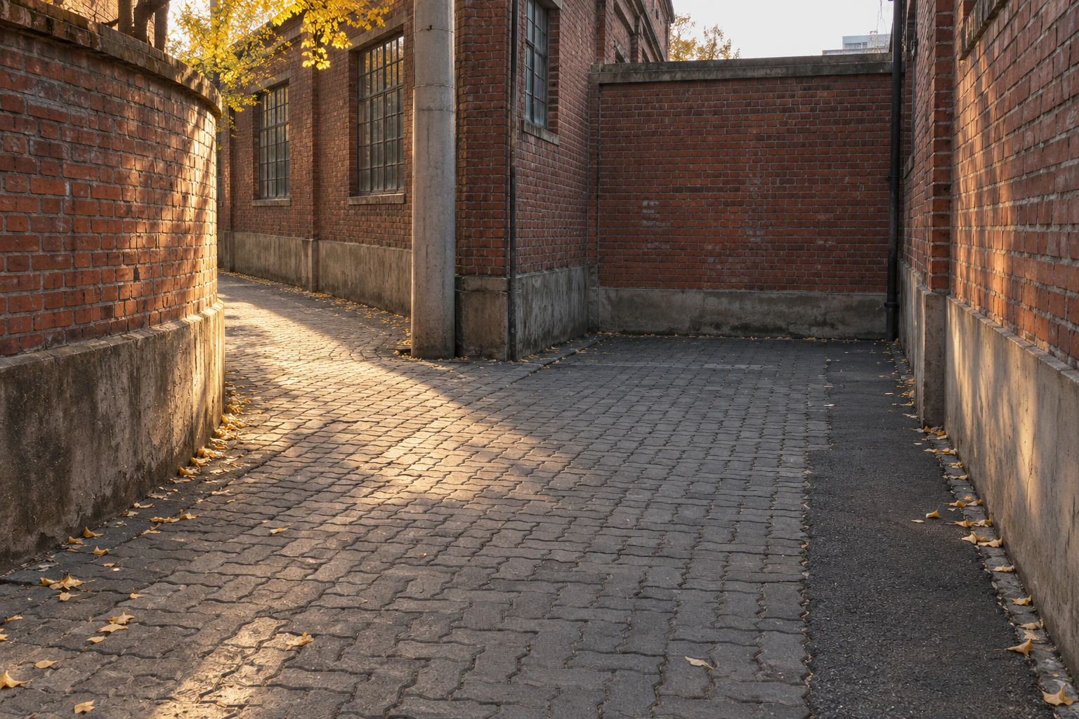 An empty Seongsu back lane of red-brick factory walls bending left past a grey utility pole, late-afternoon light falling on worn interlocking pavers, a plain brick wall closing the right side
