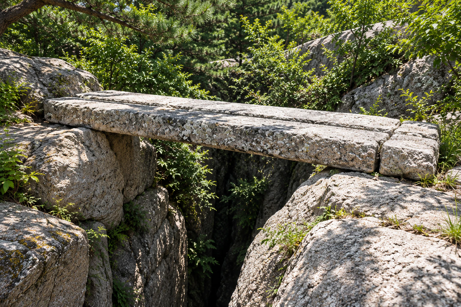 An old bridge of long dressed stones lying across a narrow cleft in the rock, seen from the side. No people. Editorial image.