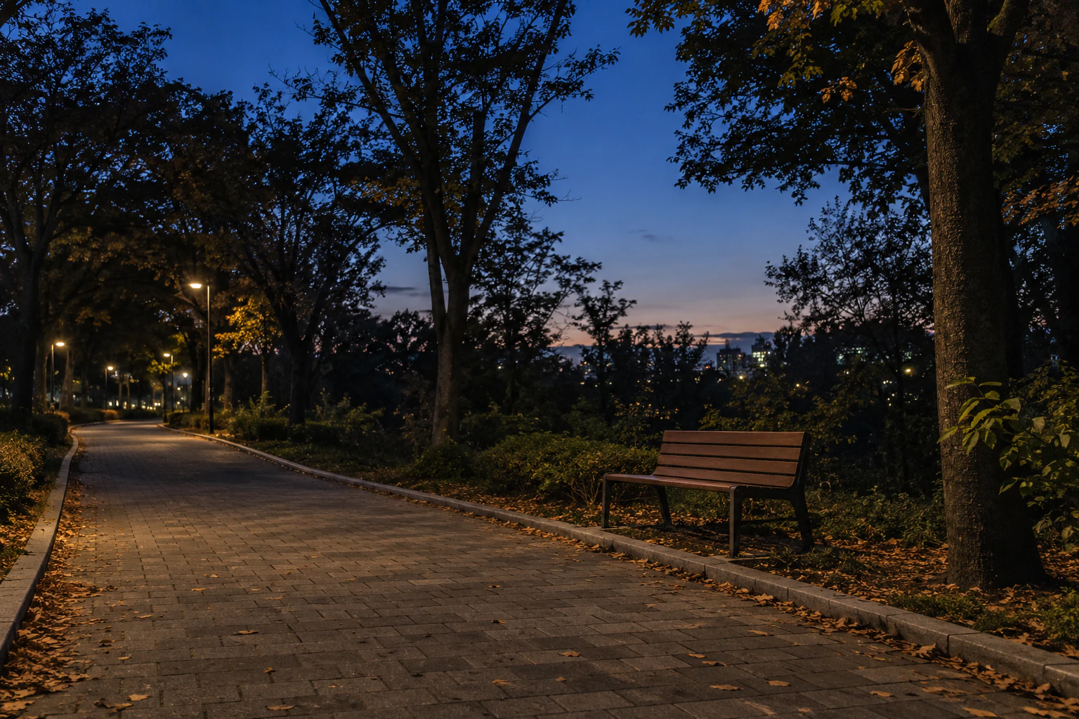 A park path at blue hour with lit street lamps, tree silhouettes and an empty bench. No people.