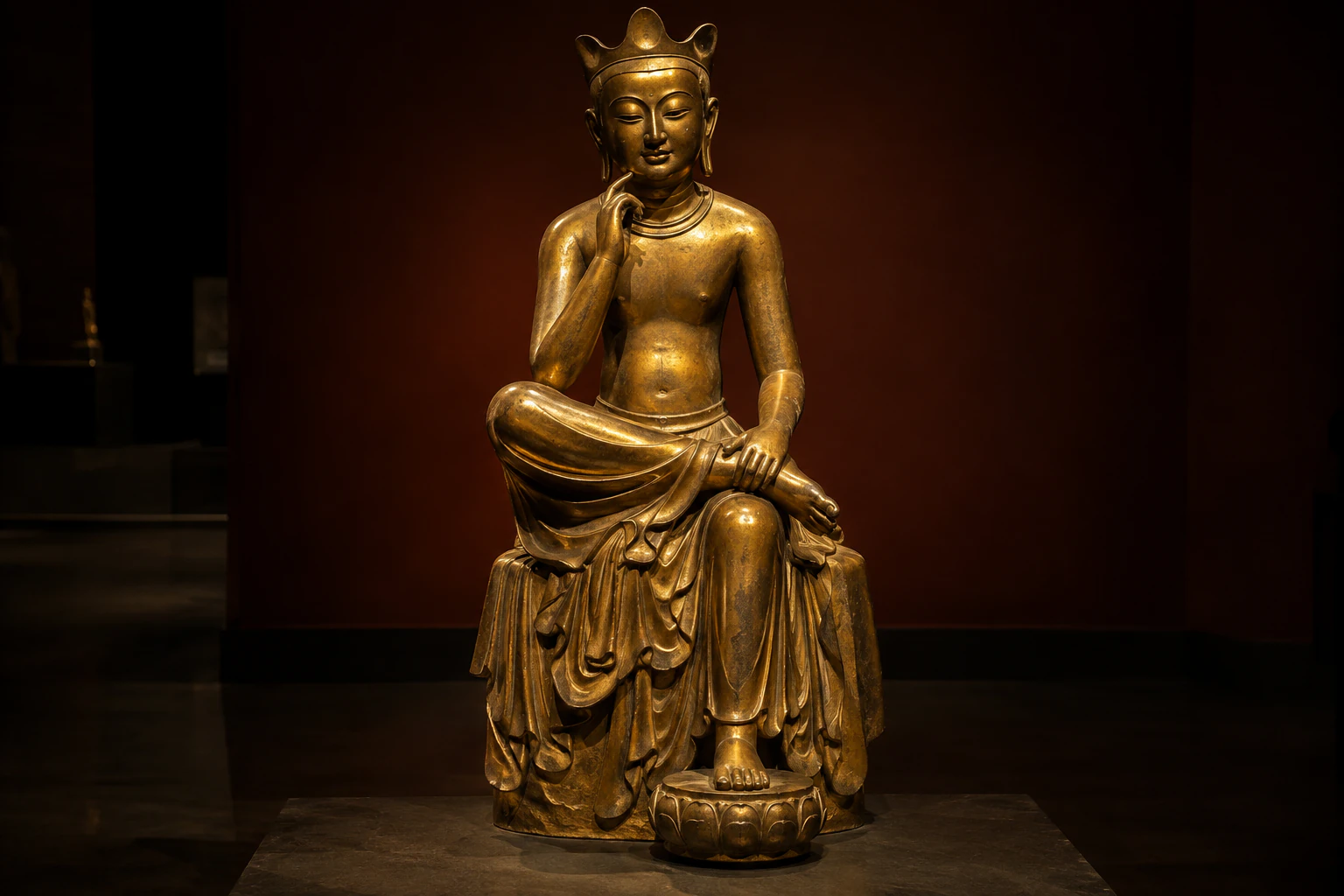 Close view of the other gilt-bronze pensive figure in the dark gallery, seated with one hand raised to the cheek. No people. Editorial image.
