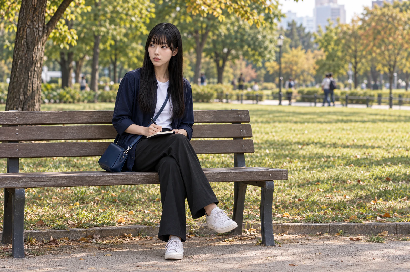 A woman sitting on a bench at the edge of a lawn, writing in a small notebook. No food. Editorial image.