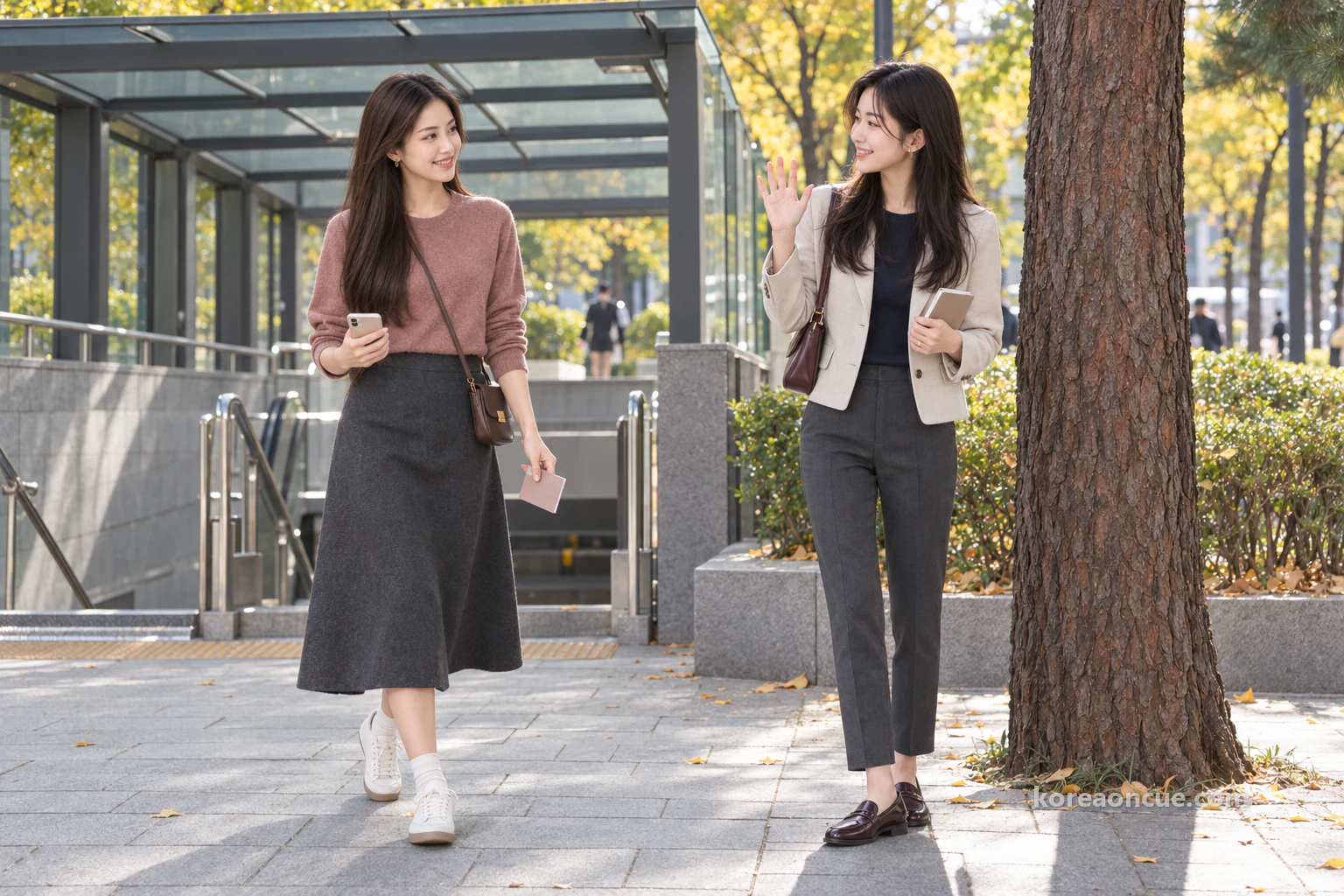 Rina waving beside a tall pine tree next to a subway exit, and Mali smiling at her as she comes out of the exit. Editorial image.