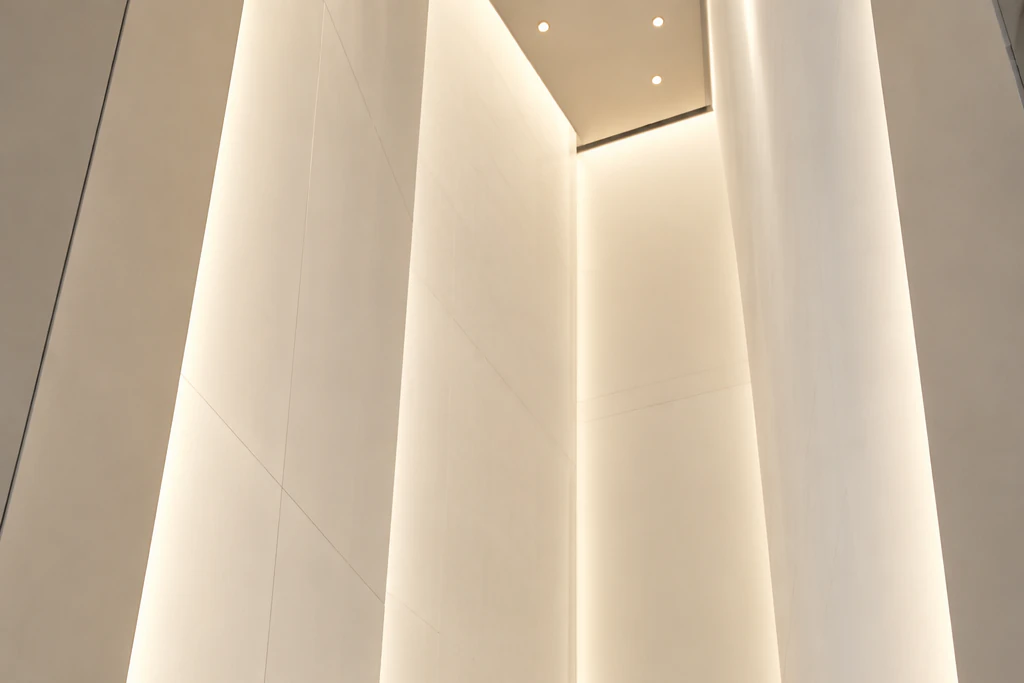 Elena seen small from behind at the entrance of a tall, narrow trapezoid-shaped exhibition space, looking up at its softly glowing inner walls. Editorial image.