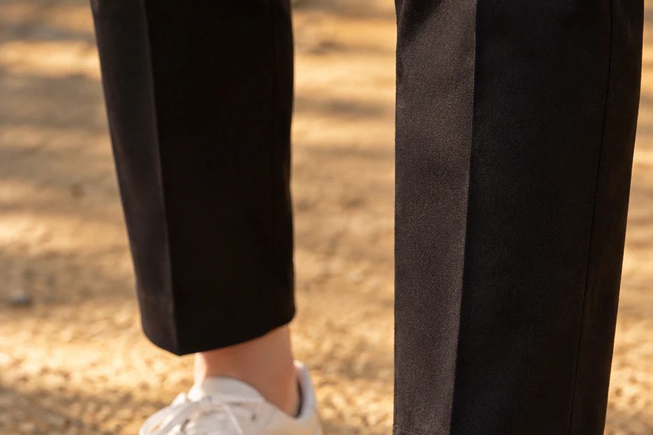 Close-up of white low sneakers and black trouser hems paused on a yellow-brown earthen path just before a step back, the grain of the soil caught in low warm light, seen at ankle height. Editorial image.