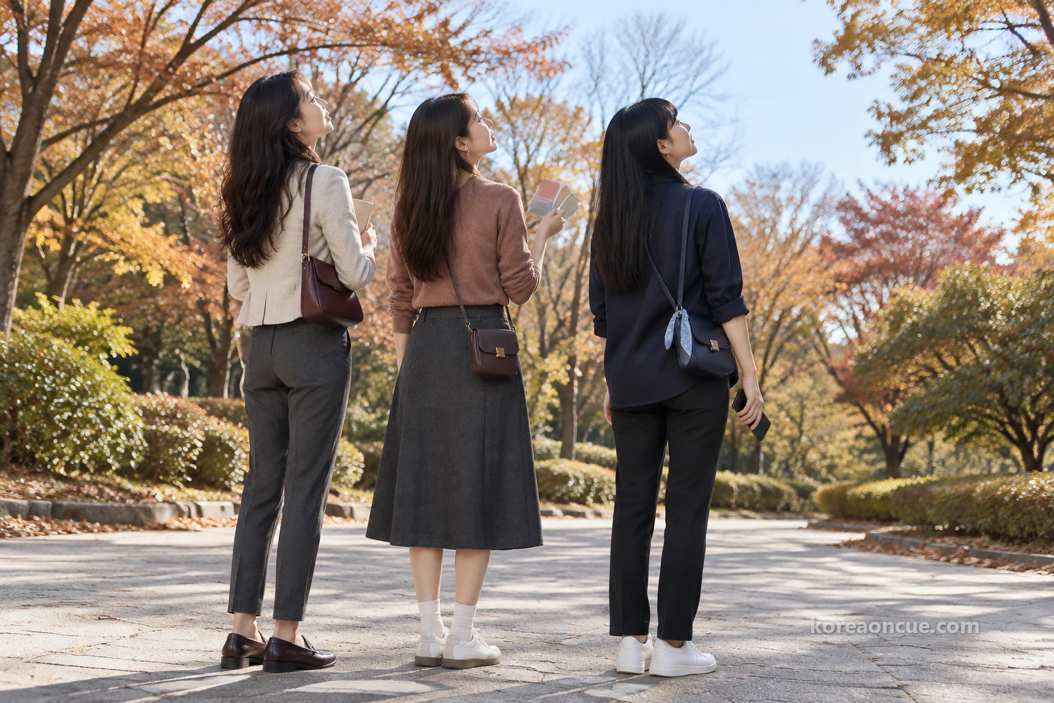 晚秋早晨在公園寬闊步道上停下腳步、抬頭望向遠處塔的 Rina、Mali 和 Maya 的斜後方身影,畫面上緣模糊地露出塔的一小部分,路旁的秋色樹木與寬闊天空。編輯示意圖。