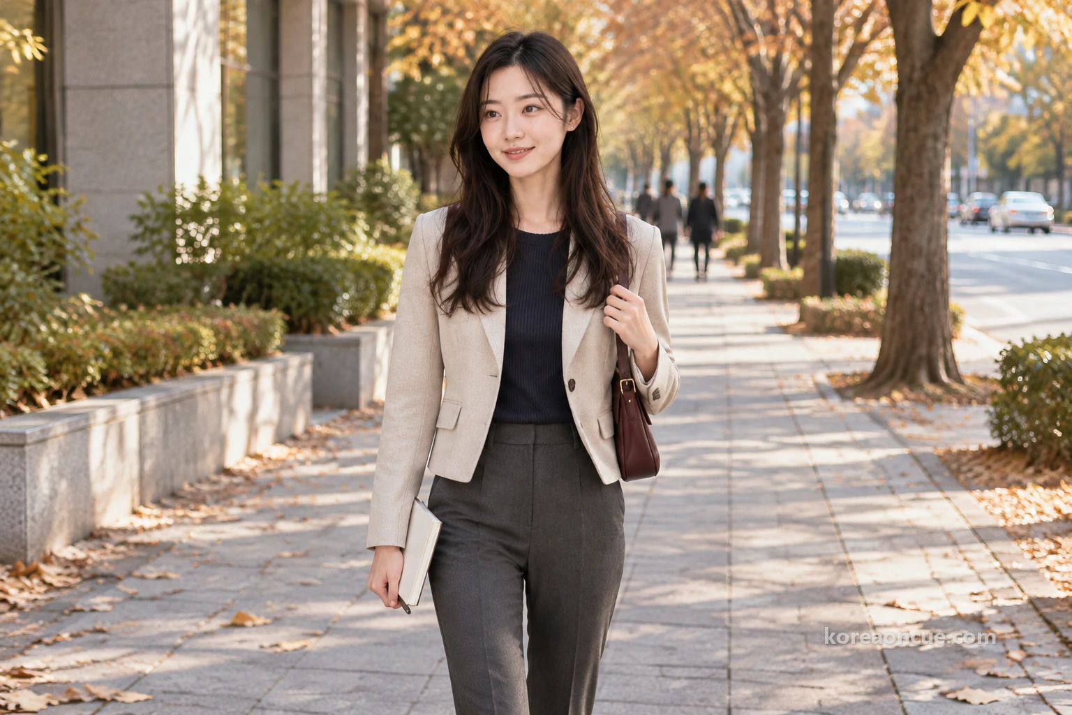 Rina seen at an angle from the front, walking alone along the wide pavement of a big city avenue on a clear late-autumn afternoon, street trees with thinning leaves and fallen leaves on the paving, a folded notebook in her right hand and her left hand on her bag strap, her eager gaze on the road ahead as it stretches far into the distance. Editorial image.