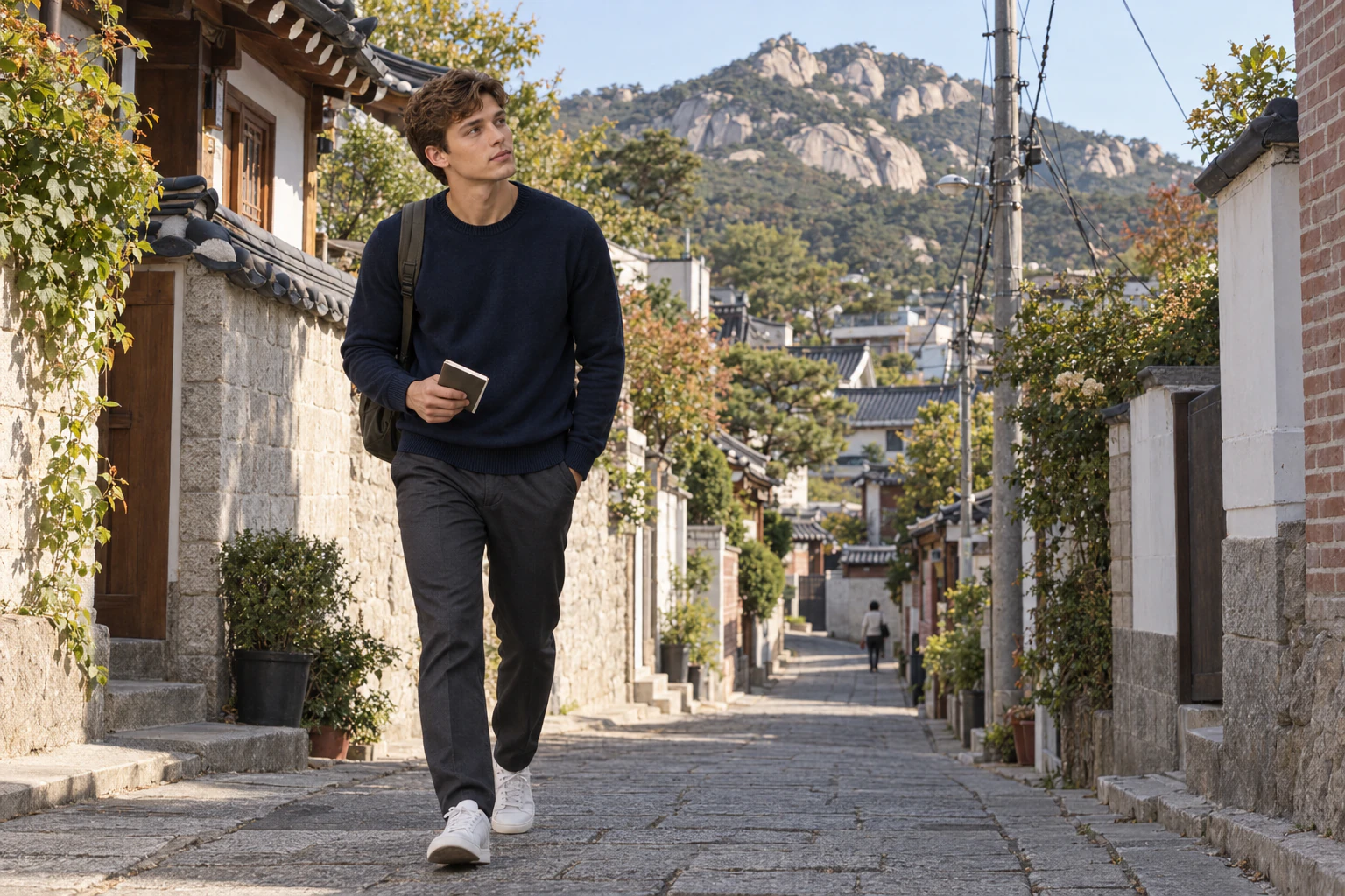 낮은 집들 사이 좁은 오르막을 걸어 올라가는 남성의 옆모습, 길 끝으로 바위산이 보인다. 편집 이미지.
